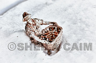 a sculture of a man sitting in the snow holding an urn of cigarette butts