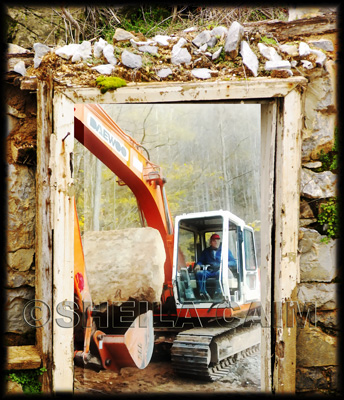 A bulldozer moving a huge rock seen through an abandoned structure